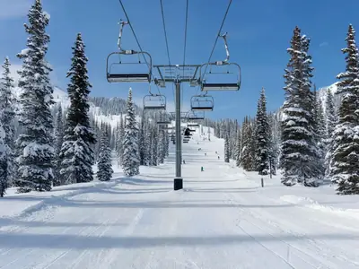 An empty chairlift rising over freshly groomed ski runs on a big mountain.