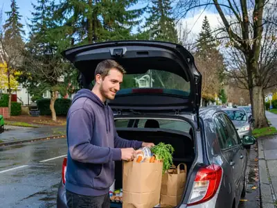 A young man loading groceries into the back of a small car-share car on a Vancouver street.
