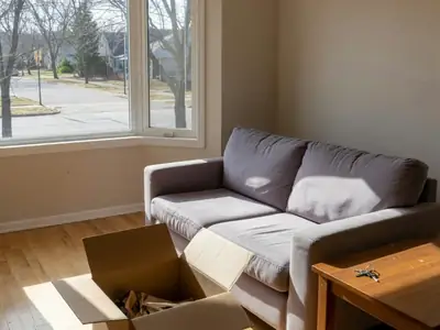 A cozy starter home living room with an open moving box, a new sofa and keys on a side table.