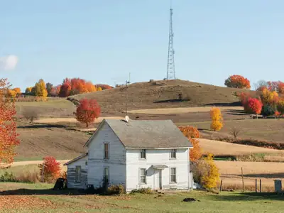 A farmhouse with a small fixed wireless antenna on the roof and a radio tower on a distant hill.