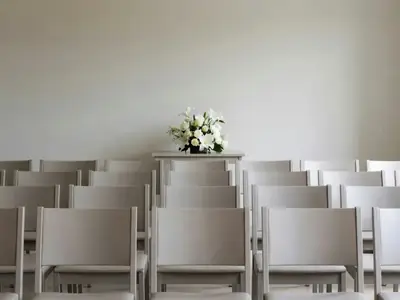 A funeral home chapel with rows of chairs and a simple flower arrangement.