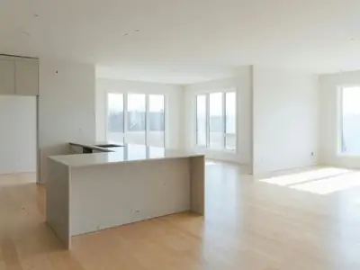 The bright open-plan main floor of a brand-new home, empty, with a kitchen island and light wood floors.