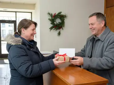 A smiling resident handing a small wrapped gift and a blank card envelope to a friendly building concierge at a lobby desk.