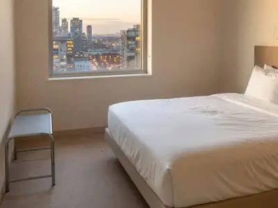 A hotel room with a made bed, a window view of the city and a small luggage rack.