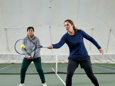 Two women playing doubles-style rallies on an indoor tennis court under a white air-supported dome.