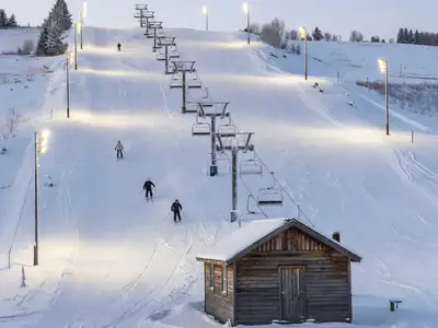 A small local ski hill lit up for night skiing, with floodlit runs and a T-bar lift.