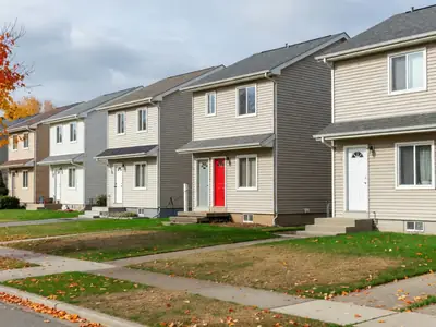 A row of similar suburban houses seen from across the street, one with a bright red door.