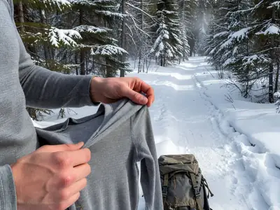 Hands pulling on a merino base layer top before a winter hike.