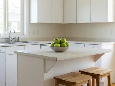 A sunlit kitchen in a house for sale, staged with a bowl of green apples and two stools at the island.