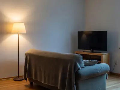A living room at night with a sofa, a blanket and a TV switched off on a stand.