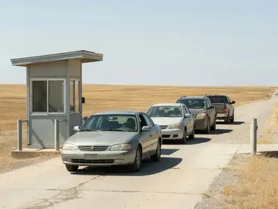 A car at a land border crossing booth with a short line of cars behind.