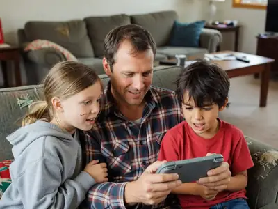 A father and two kids playing a handheld game console together on a sofa.