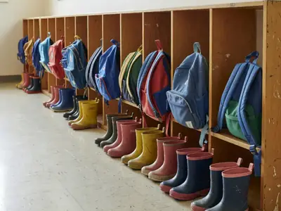 Cubbies with small backpacks and rain boots lined up in a daycare hallway.