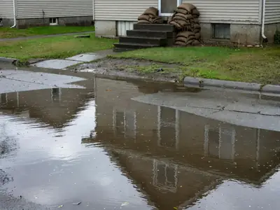 A residential street partly flooded after heavy rain, water up to the front steps of a house.