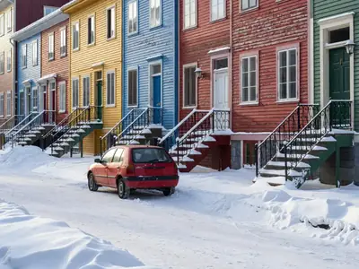 A small car parked on a snowy street lined with colourful row houses.