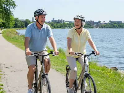 A retired couple in their early sixties cycling on a paved lakeside path.