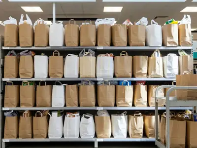 A row of filled grocery bags waiting on shelves in a supermarket online-order pickup area.