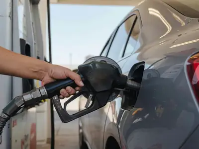 A hand lifting a fuel nozzle from a gas pump beside an open fuel door.