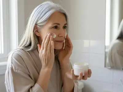 A woman in her late fifties applying moisturiser at her bathroom mirror.