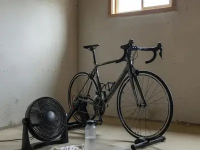 A road bike mounted on a smart trainer in a basement corner with a fan.