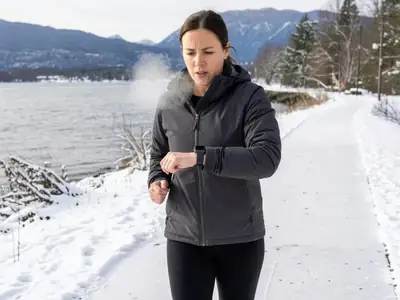 A runner in winter running gear glancing at a plain smartwatch on her wrist while jogging.