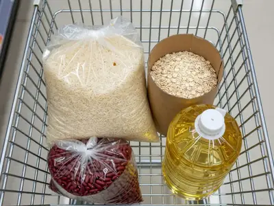 A grocery cart holding a bag of rice, dried beans, oats and a jug of cooking oil.