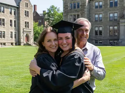 A new graduate in a gown and cap hugging her parents outside on a sunny day.