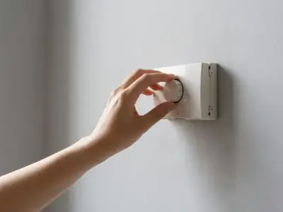 A hand adjusting a wall thermostat dial in a condo hallway.