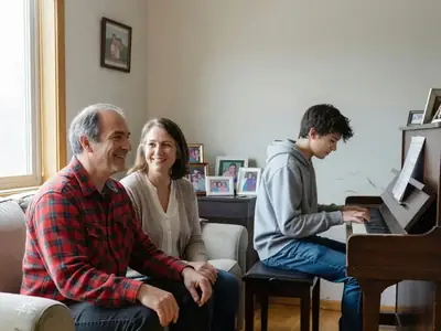 A middle-aged couple watching their teenage son practise piano in the living room, smiling proudly.
