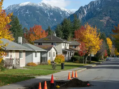 A residential street of houses with mountains in the background and fibre utility work on the boulevard.