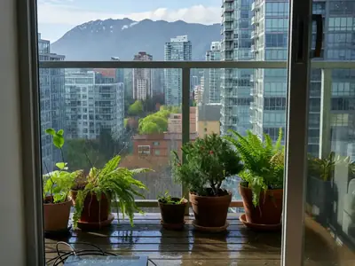 A Vancouver condo balcony view of glass towers and mountains with a plain router inside the doorway.