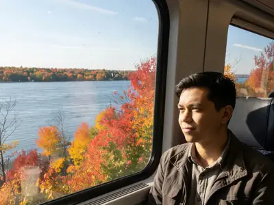 A passenger in a train window seat watching the St. Lawrence River pass by.