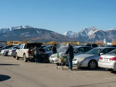 A supermarket parking lot with mountains on the horizon, a few shoppers loading cars.