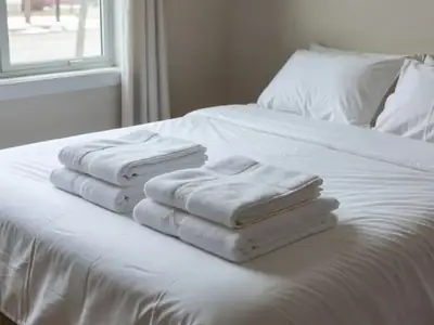 A neatly made bed with crisp white sheets and folded towels stacked at the foot.