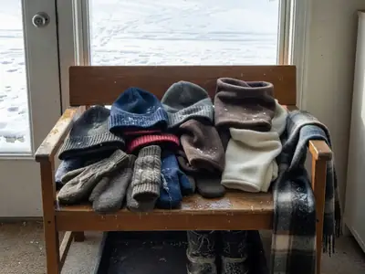 A wooden bench in a home entryway with a jumble of knitted toques, wool mitts, fleece neck warmers and a scarf.