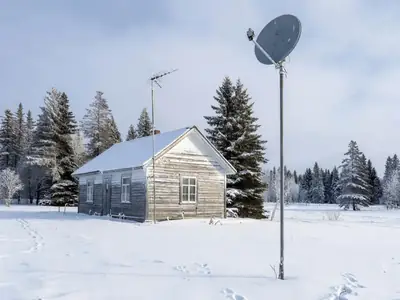A rural property in winter with a satellite dish on a pole and a fixed wireless antenna on the house.