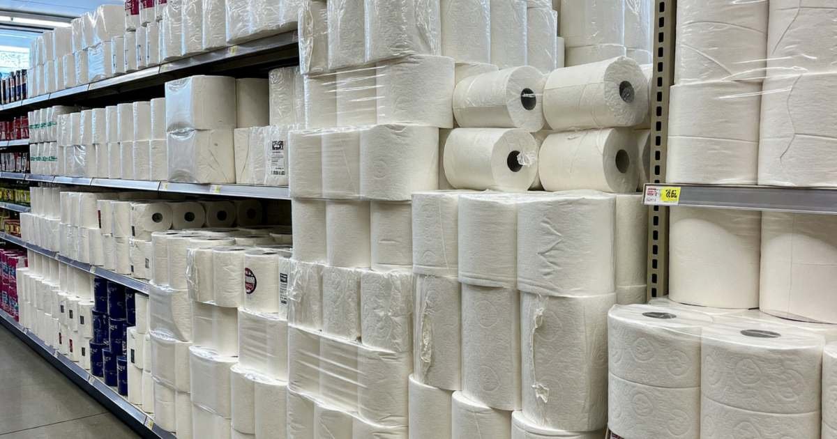Bulk packs of toilet paper and paper towels stacked in a supermarket aisle, illustrating comparing toilet paper and paper towel unit prices.
