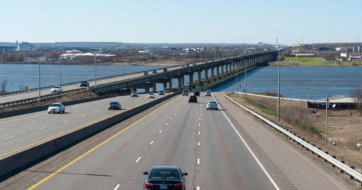 A car on a highway approaching a long bridge over a river at a border city, illustrating US trips from Canada, fly, drive or cross the border.