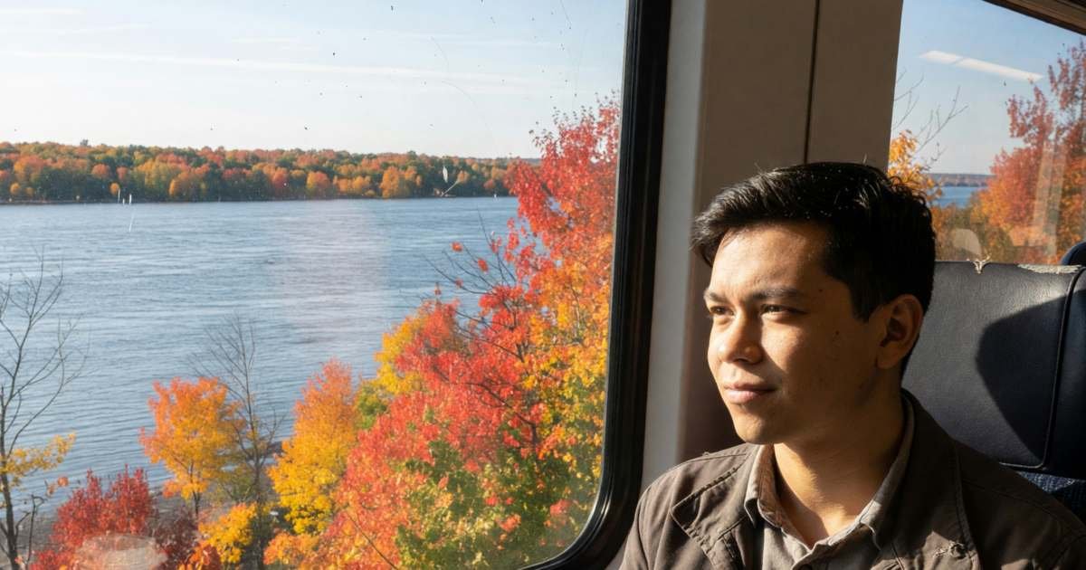 A passenger in a train window seat watching the St. Lawrence River pass by, illustrating Via Rail versus driving the Québec–Windsor corridor.