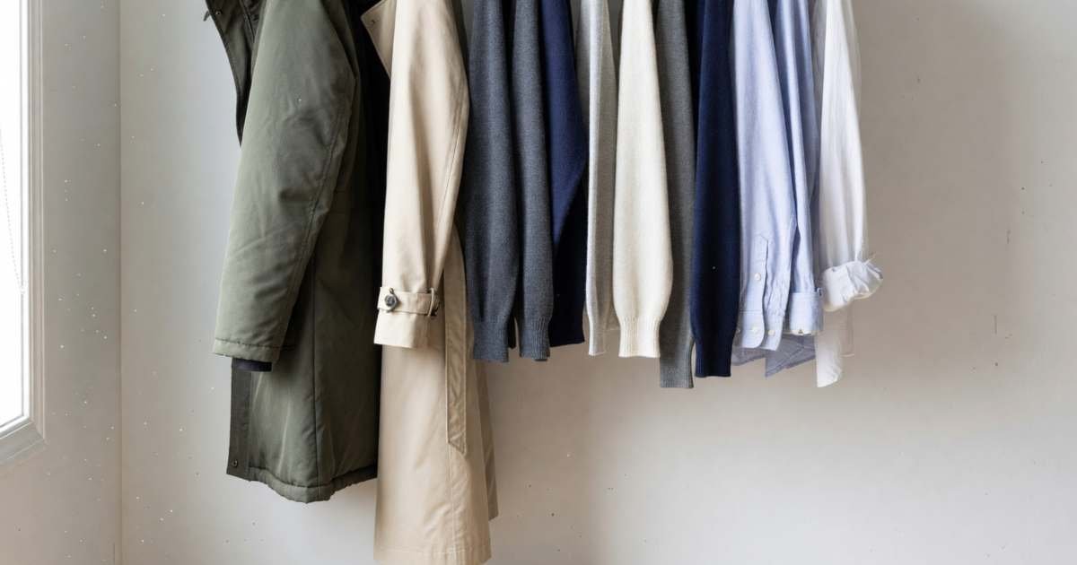 A minimalist capsule wardrobe on an open rail, a parka, a trench coat, sweaters and a few shirts, illustrating a four-season Canadian capsule wardrobe.