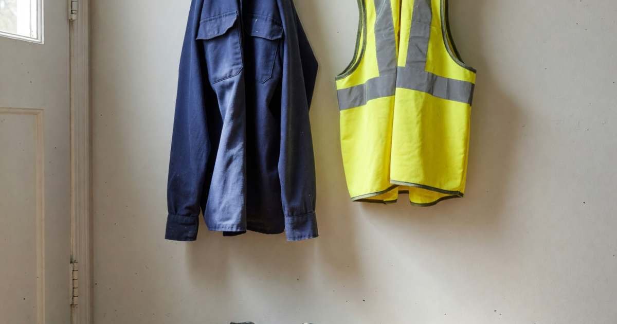 A uniform shirt, steel-toe boots and a hi-vis vest hung on hooks by a back door, illustrating whether you can write off work clothes in Canada.