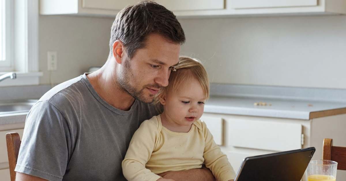 A toddler and her father watching a video on a tablet propped on the kitchen table, illustrating YouTube Premium Family in Canada.